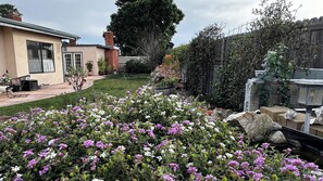 Een woon tuin met een terras, een kleine vijver en verschillende bloeiende planten.