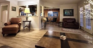 A living room with a brown leather sofa, a coffee table, and a dining area with chairs and a chandelier. - Bay Ho Retreat—Sleeps 9—5-Minutes to La Jolla, Pacific Beach, Bay & Trolley (San Diego)