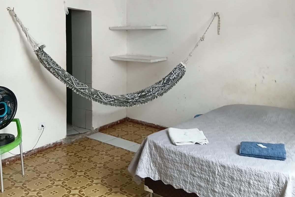 Una habitación con una cama, una hamaca, una silla verde y un ventilador.