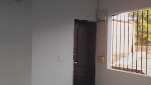 Una habitación con piso de baldosas, una puerta oscura y una ventana con barrotes.