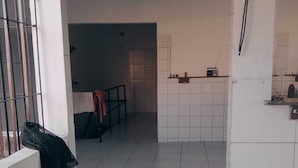A corridor with a tiled floor leading to a kitchen area with white tiles and a window with metal bars.