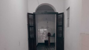 A narrow hallway with a tiled floor leading to a room with a tiled wall and a door with a metal gate.