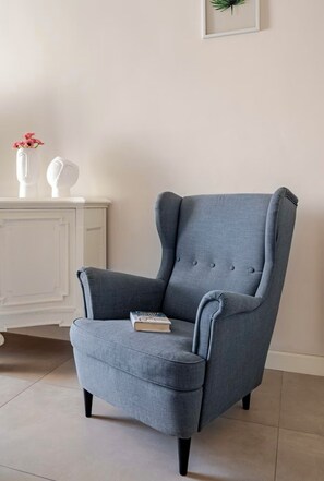 Un sillón tapizado gris con un libro encima, ubicado en una habitación con un aparador blanco y un cuadro en la pared.