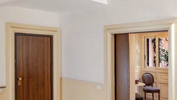 Una escalera con barandilla de madera y balaustres de metal, que conduce a una habitación con puerta de madera y una pequeña mesa con una silla.