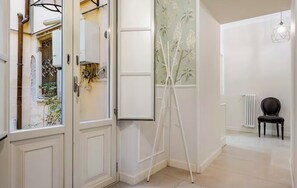 Un pasillo con una puerta blanca, un trípode, un radiador y una silla.