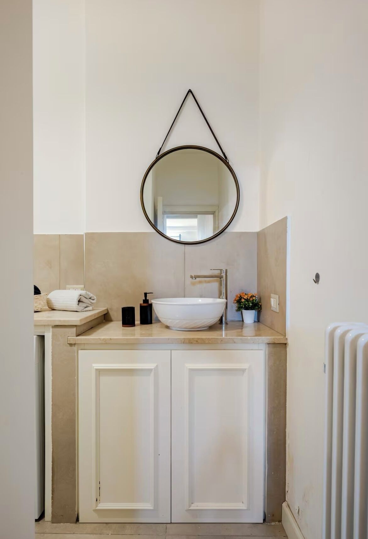 A bathroom with a white sink, a round mirror, and a towel on the counter.