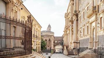 Una calle adoquinada flanqueada por edificios históricos con fachadas ornamentadas y un arco central que conduce a una estructura con cúpula.