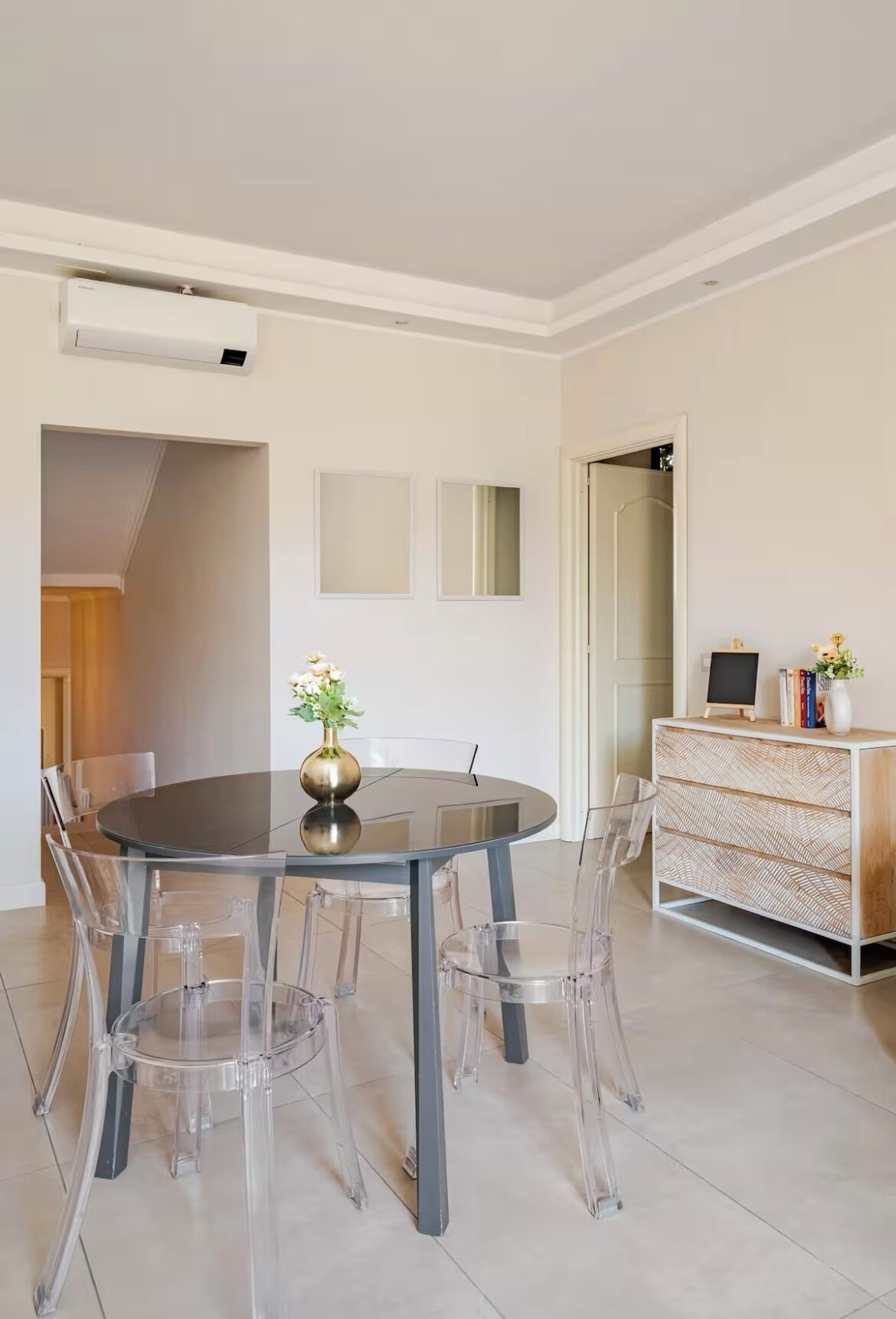 Uma área de jantar moderna com mesa redonda, cadeiras transparentes e um vaso de flores.