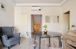 Un comedor con una mesa redonda, sillas transparentes, un sofá gris y un jarrón pequeño con flores.