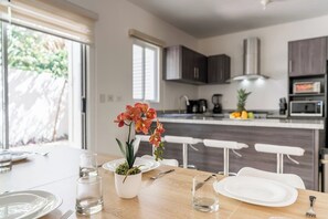 A dining area with a table set for two, a potted orchid, and a kitchen in the background. - Spacious 3BR Home in Pla del Carmen (Playa del Carmen)