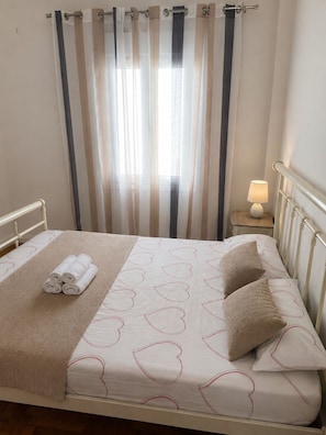 A bed with a patterned bedspread, rolled towels, and a bedside lamp. - Cosy family apartment at the centre of Chora Naxos (Naxos)