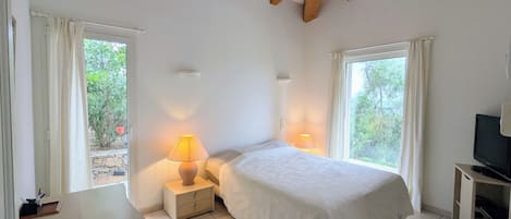 Un dormitorio con cama, lámparas de noche, televisor y ventana con cortinas.