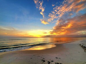 Een strand met voetafdrukken die naar het water leiden, een heldere lucht en een ondergaande of opgaande zon.