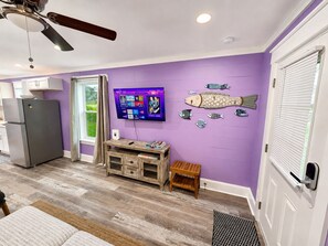 Ein Zimmer mit lila Wand, Deckenventilator, flachbildfernseher an der Wand und Kühlschrank.