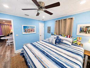 Een slaapkamer met een bed, een plafondventilator, een deur en een raam met gordijnen.
