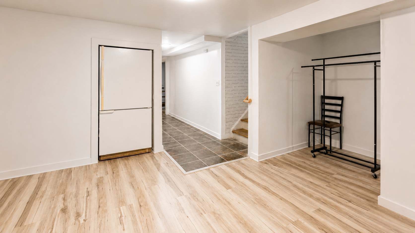 A room with a wooden floor, a white door, and a black metal rack.