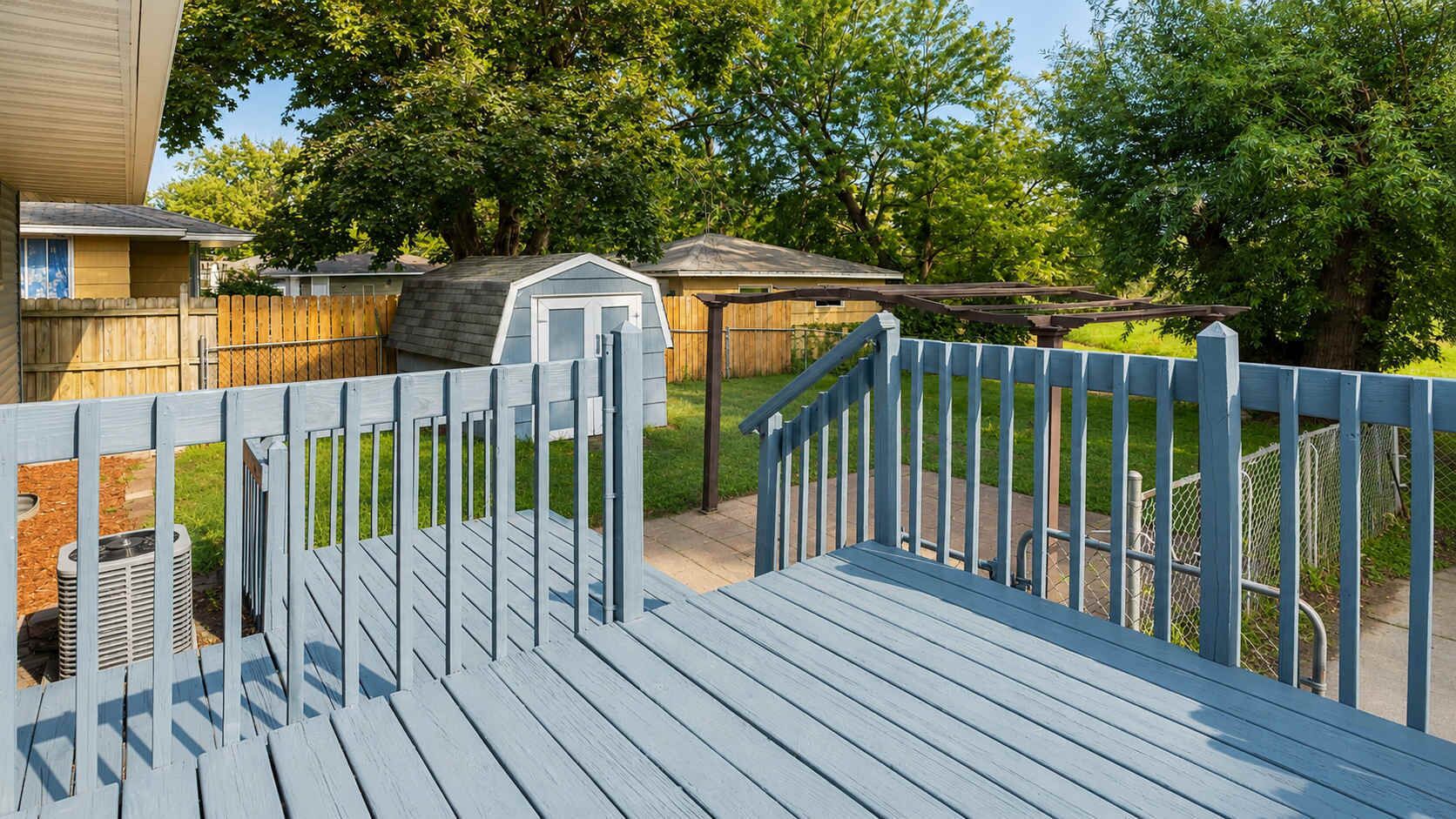 A wooden deck with a blue railing, a small shed, and a chain-link fence in a residential backyard.