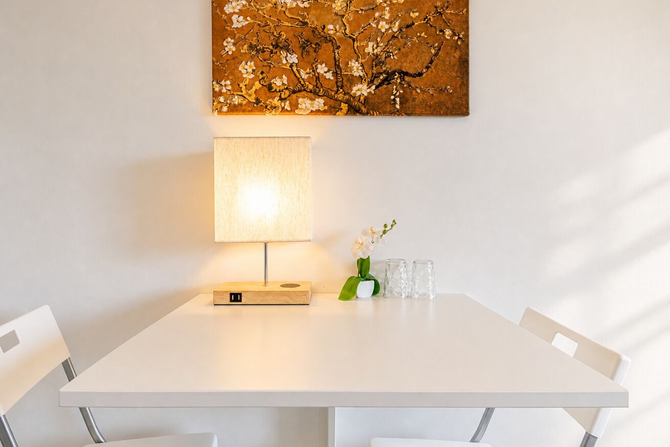 Een witte eettafel met een lamp, een bloemenvaas en twee glazen.
