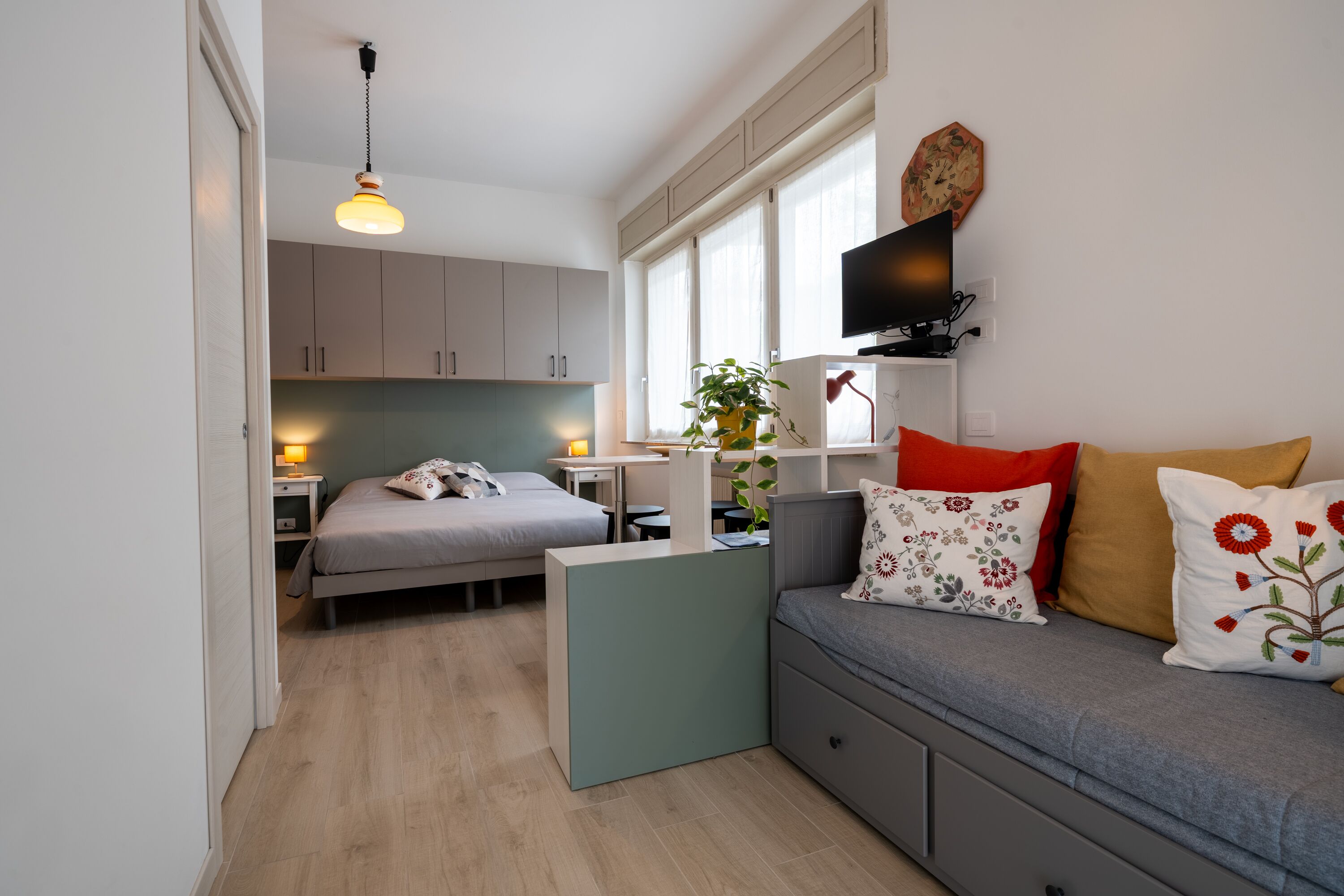 Ein gemütlicher Wohnraum mit Bett, Sofa, kleinem Tisch und an der Wand befestigtem Fernseher.