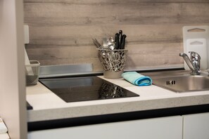 A kitchen counter with a stainless steel sink, a black induction cooktop, and a utensil holder with knives and spoons. - Two-bedroom apartment near the historic center (Verona)