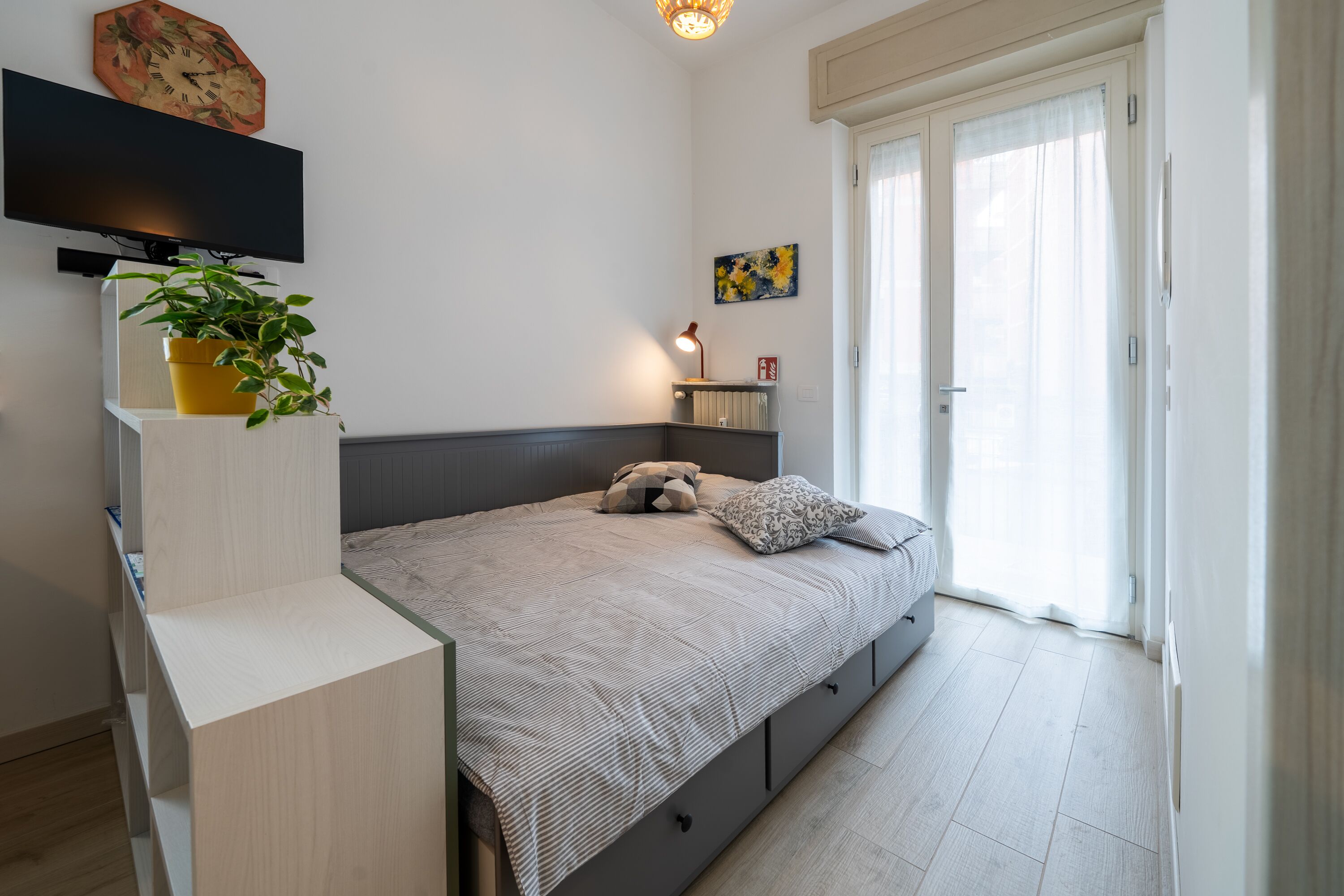 A modern bedroom with a bed, bedside table, TV, and a plant.