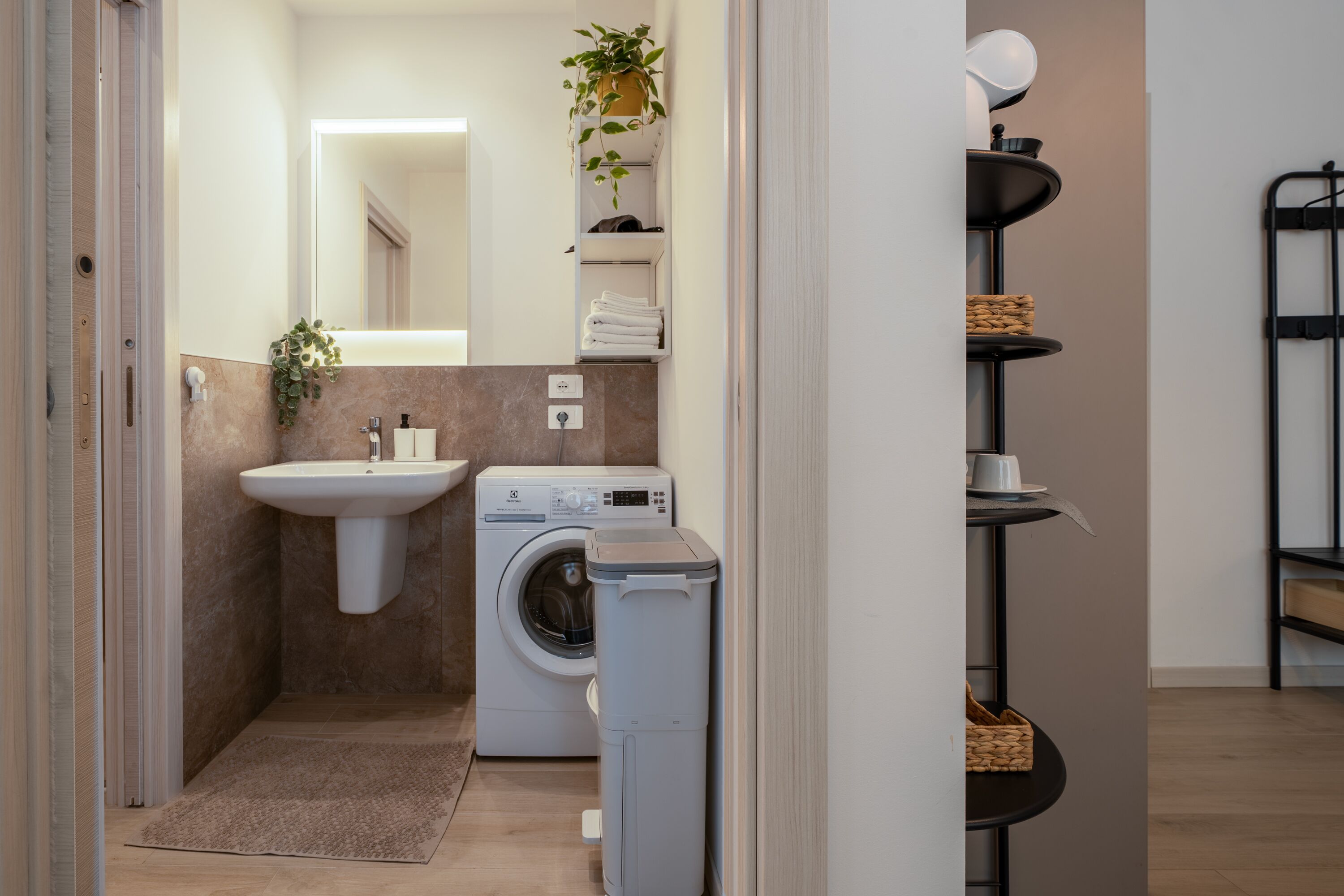 A compact bathroom with a sink, washing machine, and a small shelf with towels.