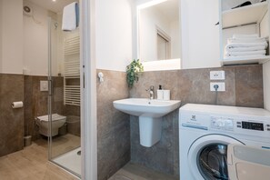 A modern bathroom with a glass shower enclosure, a white sink, a washing machine, and a mirror. - Two-bedroom apartment near the historic center (Verona)