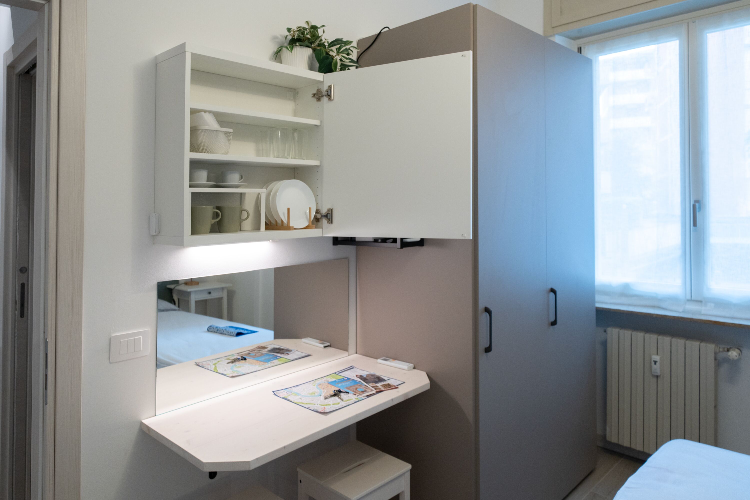 A bedroom with a bed, a desk with a map, a wardrobe, and a window.