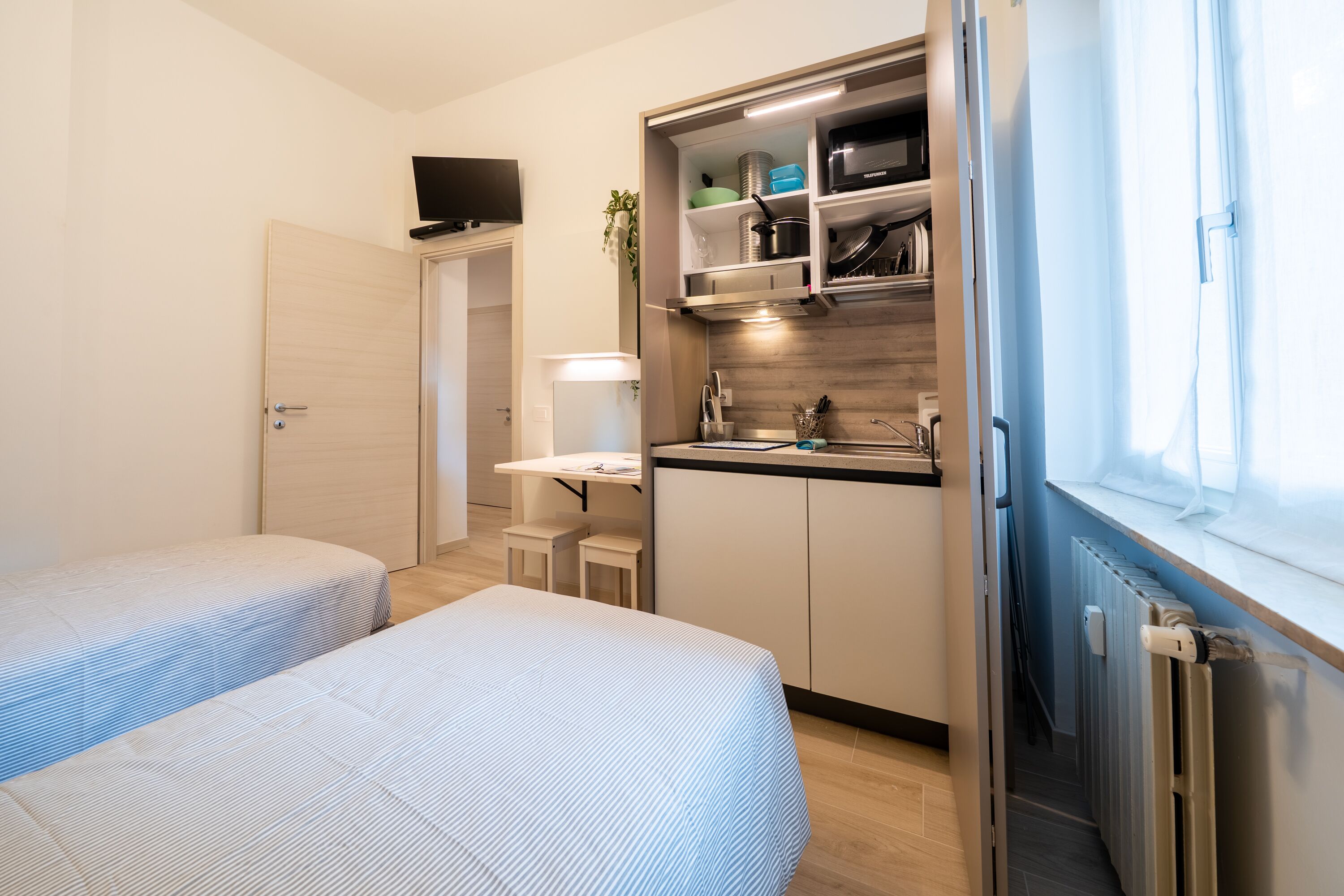 A compact room with two beds, a small kitchenette, and a window.