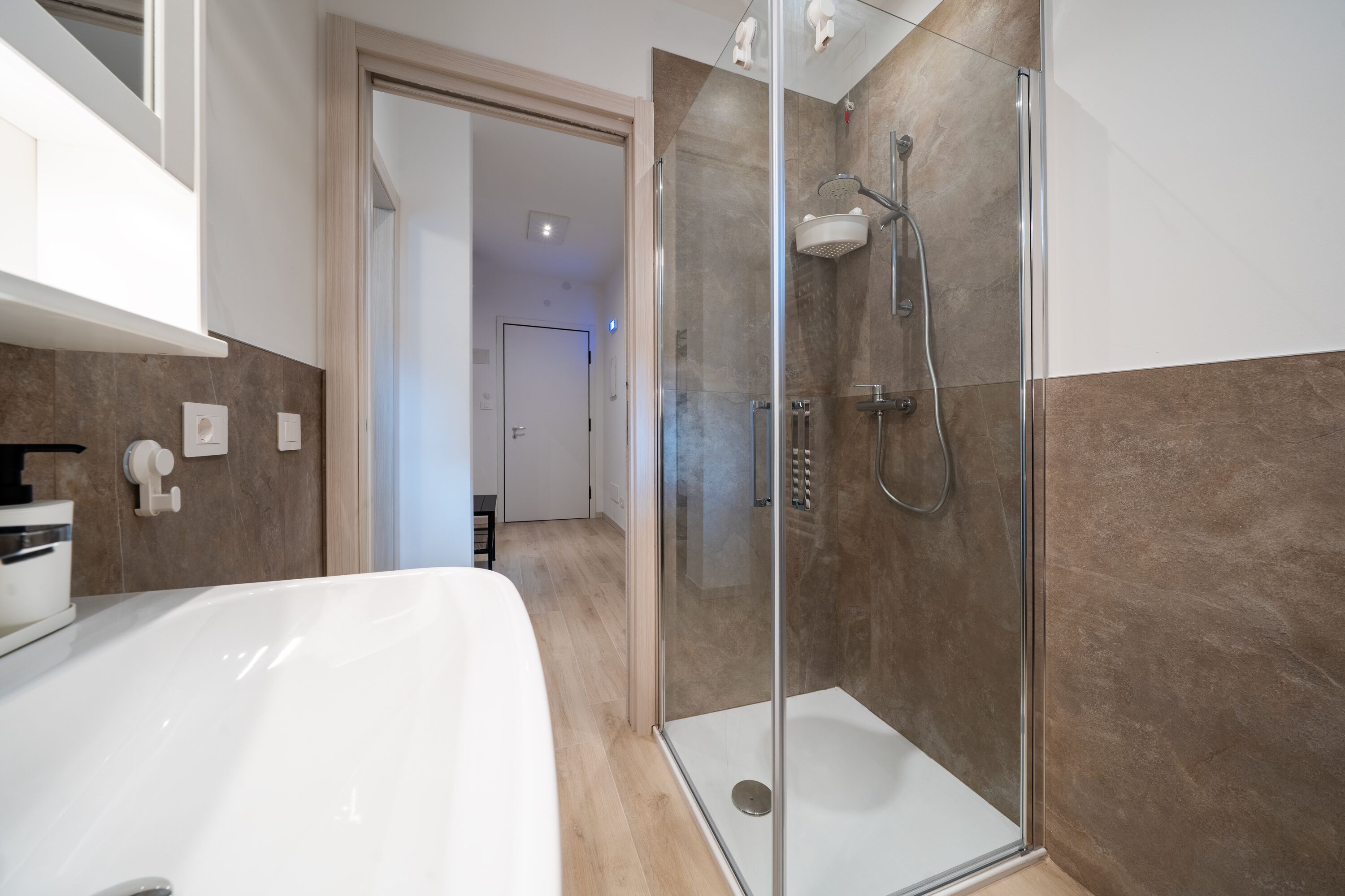 Ein modernes Badezimmer mit einer gläsernen Duschkabine, einer weißen Badewanne und Holzboden.