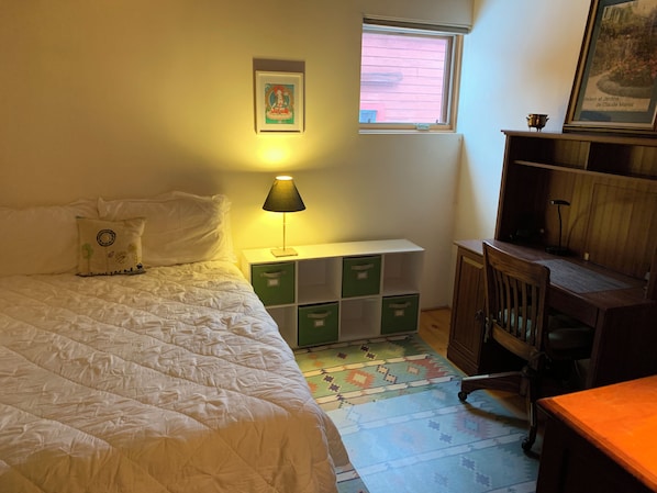 A bedroom with a bed, a bedside lamp, a window, a desk, and storage units.
