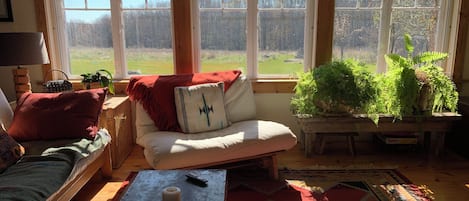 A cozy living room with a sofa, a coffee table with a candle, and a view of a garden through large windows.