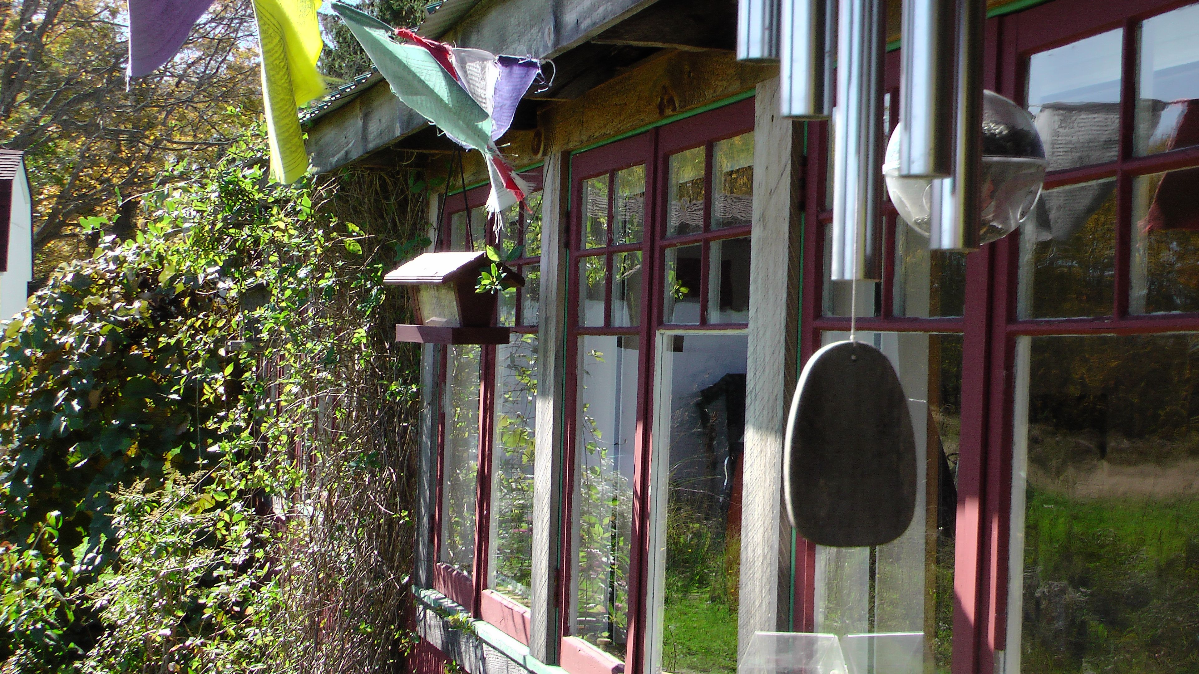 Un bâtiment avec un cadre de fenêtre rouge, une cloche suspendue et un abreuvoir à oiseaux.