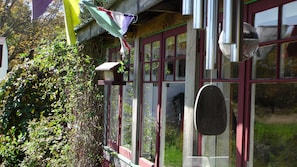 A building with a red window frame, a hanging bell, and a bird feeder.