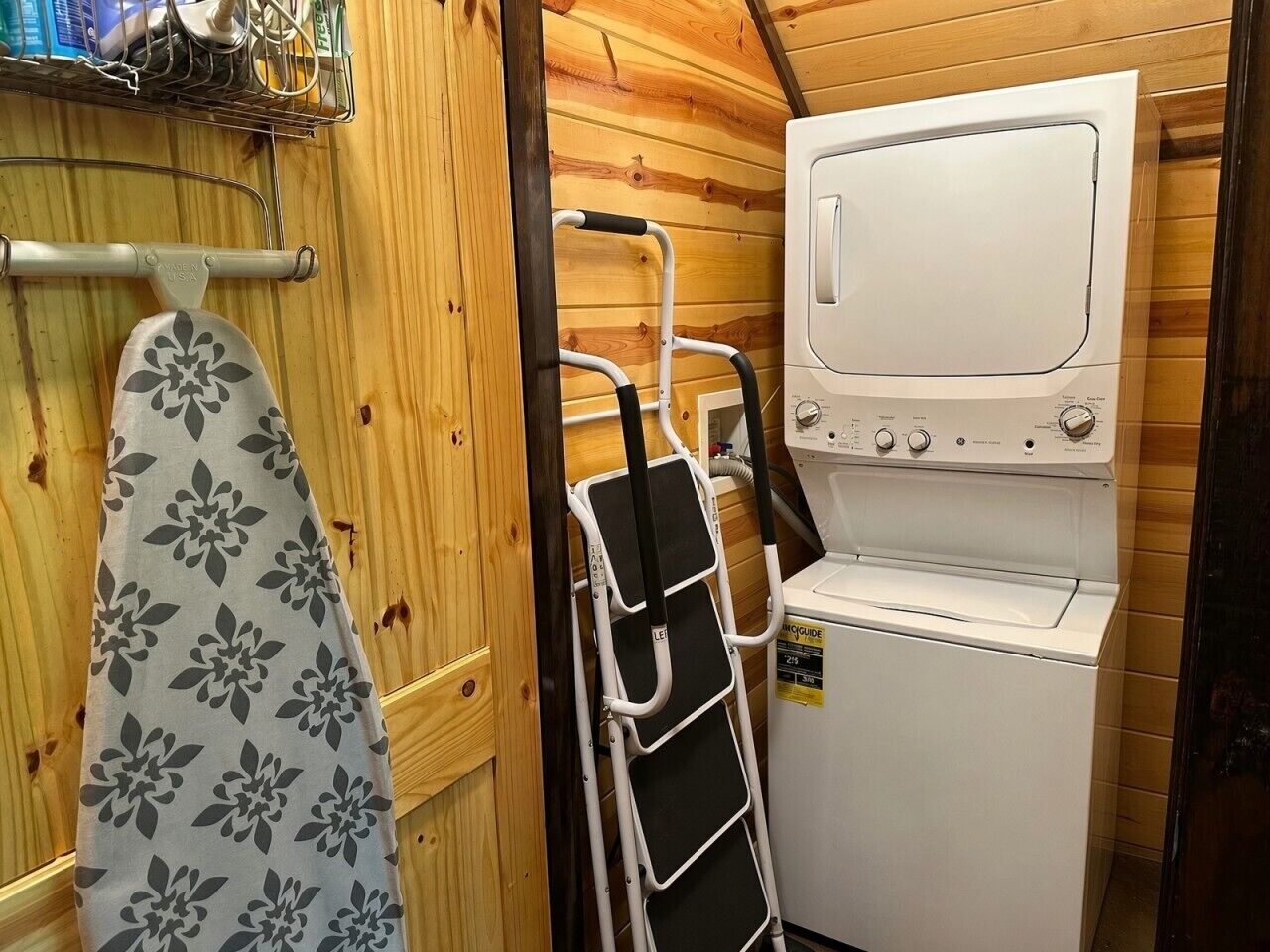 A compact laundry area with a washing machine, a drying rack, and a towel hanging on a wooden wall.