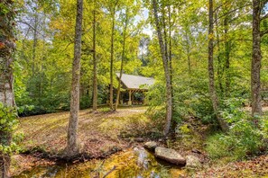 A forested area with a wooden structure, a stream, and a picnic table. - 2 King Ensuites on first level | Private with easy access | Outdoor Fireplace | Hot Tub | Game Room (Sevierville)