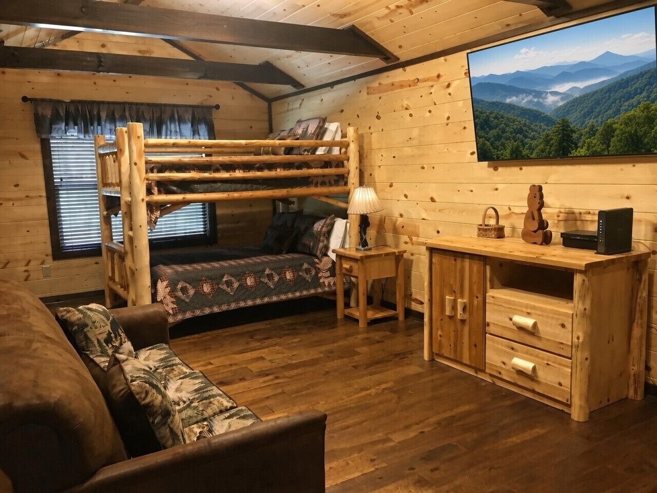 A cozy cabin interior with a bunk bed, a desk with drawers, a lamp, and a large window with a mountain view.