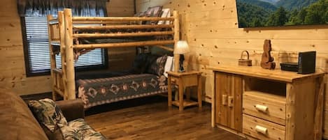 Interior acogedor de una cabaña con una litera, un escritorio con cajones, una lámpara y un amplio ventanal con vistas a la montaña.