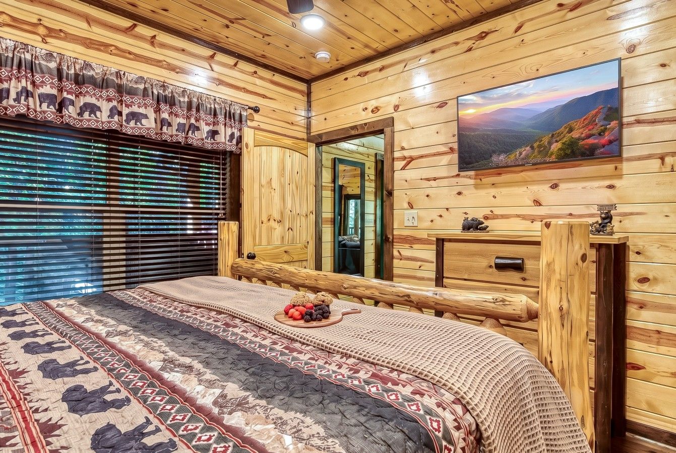 Une chambre dans un chalet en bois, avec un lit, une télévision et une fenêtre équipée de stores.
