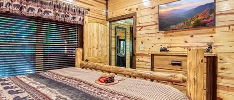 A wooden cabin room with a bed, a television, and a window with blinds.