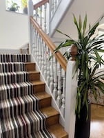 Una escalera con alfombra a rayas y peldaños de madera, balaustres blancos y barandilla de madera.