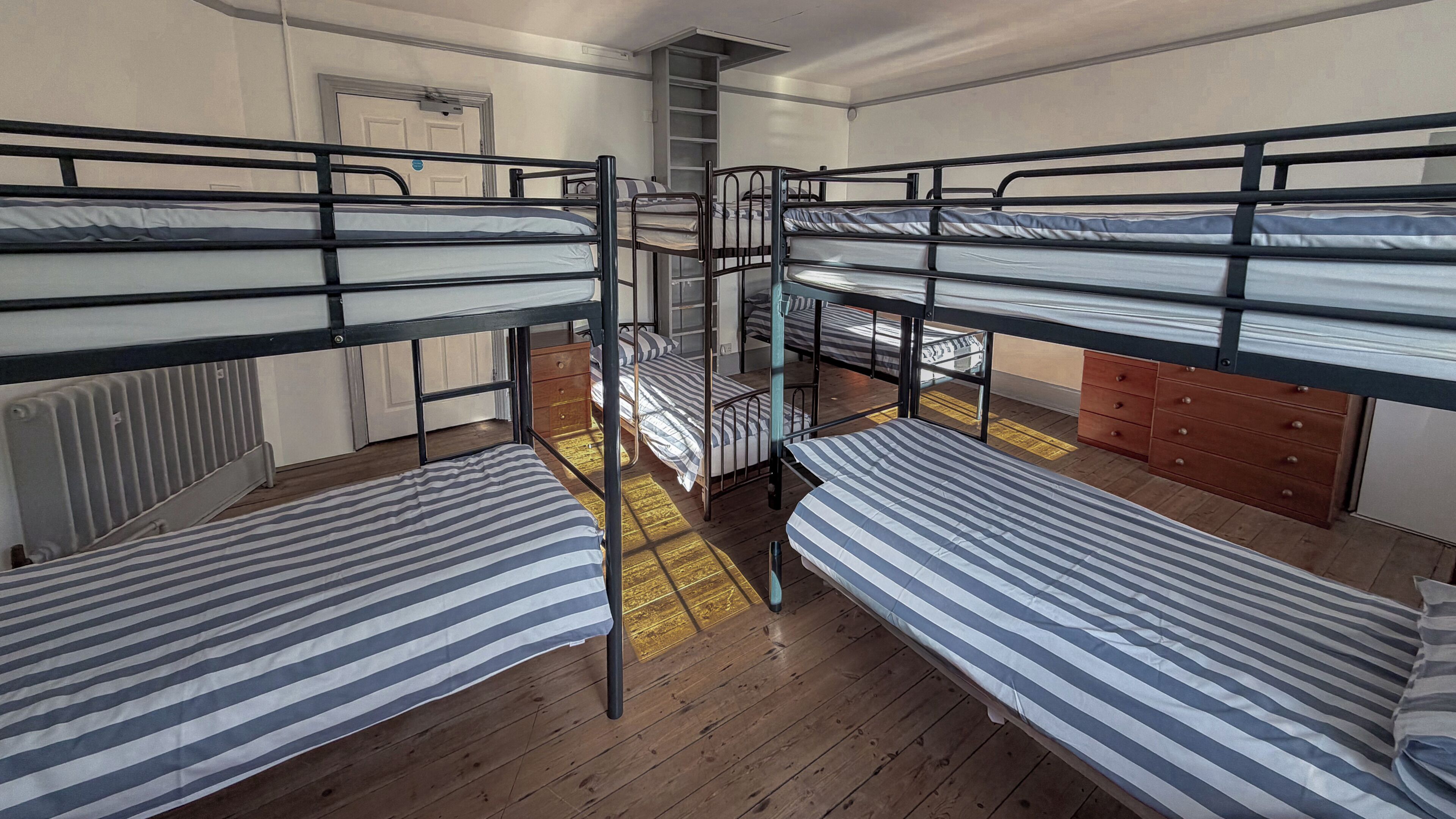 Ein Schlafsaalzimmer mit Etagenbetten, Holzboden, Heizkörper und einer Tür.