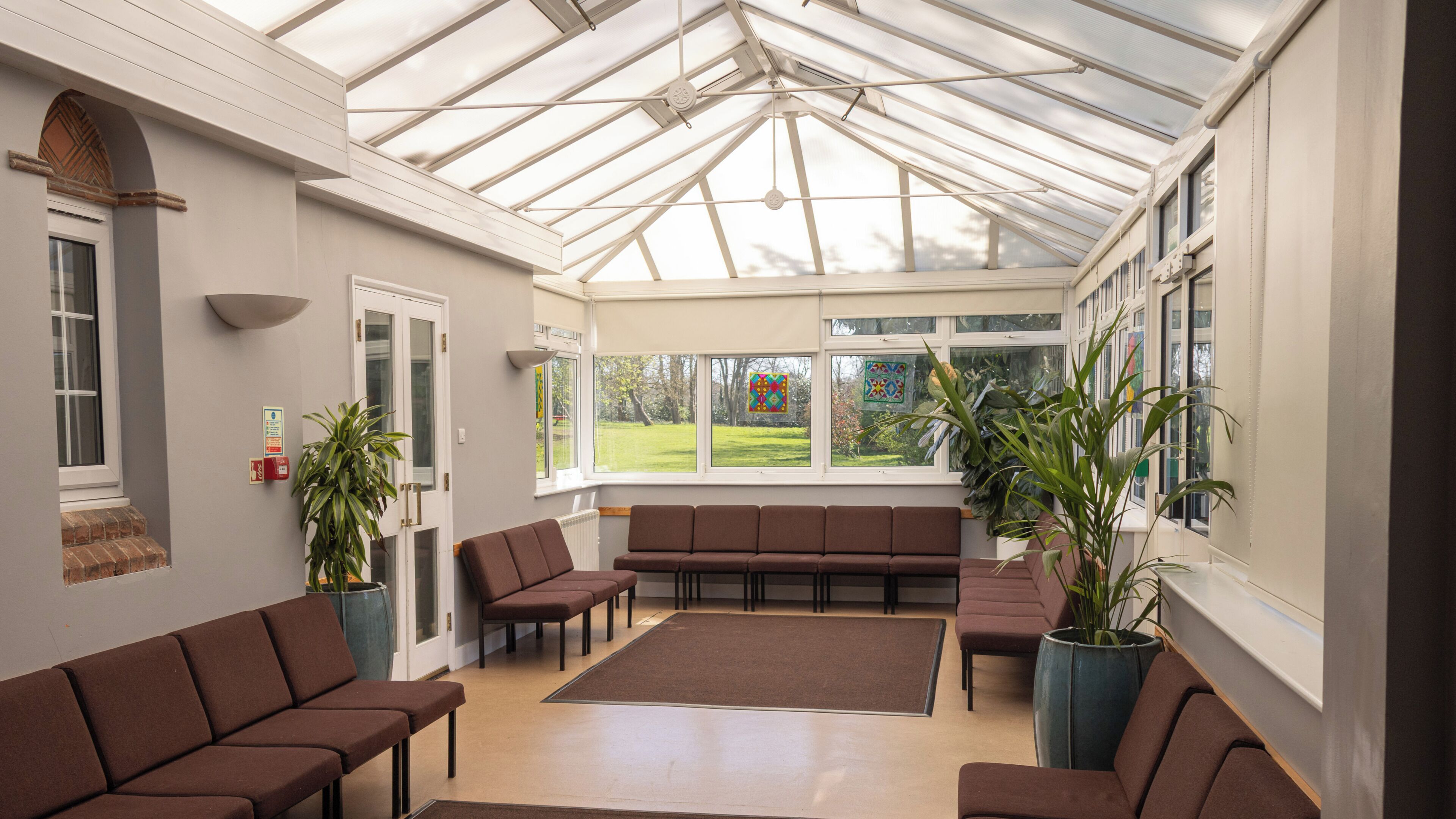A conservatory with seating, large windows, and potted plants.