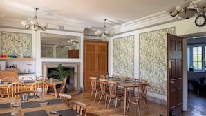 A dining area with wooden tables and chairs, a fireplace, and patterned wallpaper.