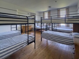 Un dormitorio con literas, pisos de madera, un aparador y una ventana con cortinas.
