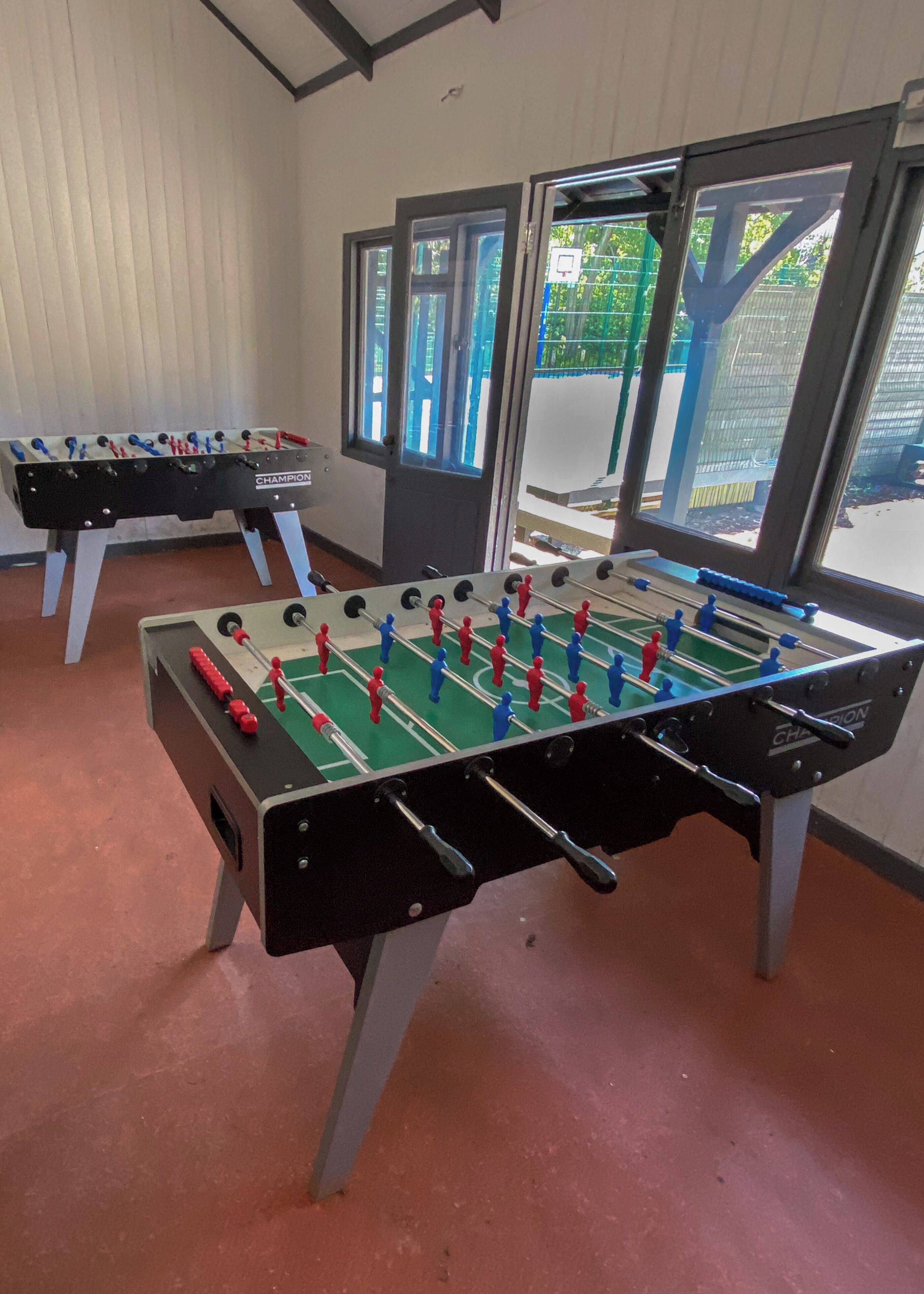 Two foosball tables in a room with windows and a view of the outdoors.