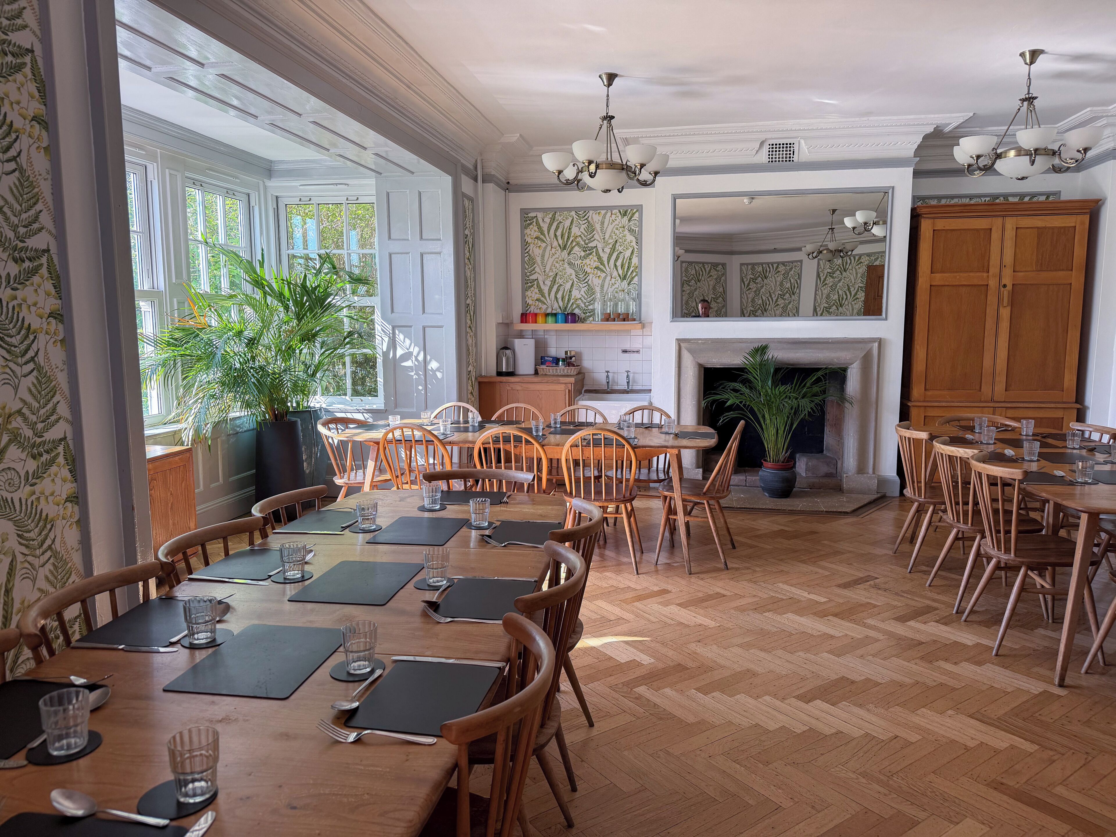 A dining area with wooden tables and chairs, a fireplace, and a kitchen in the background.