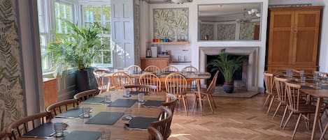 A dining area with wooden tables and chairs, a fireplace, and a kitchen in the background.