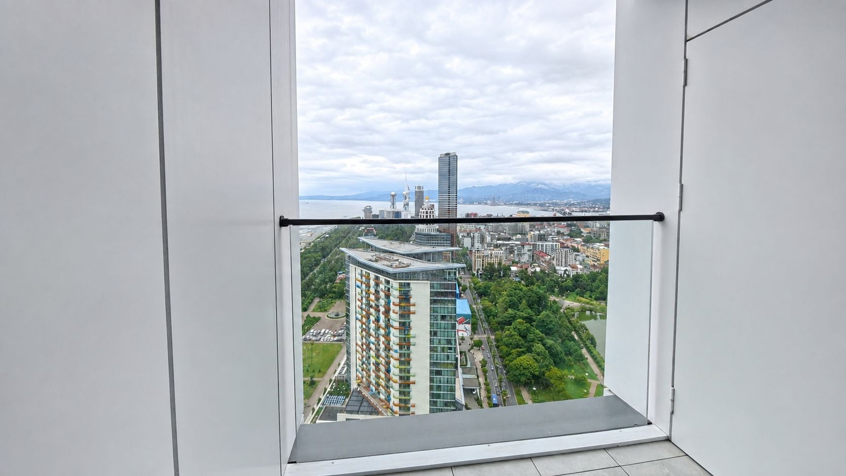 A view from a window with a metal frame, overlooking a cityscape with buildings and a river.