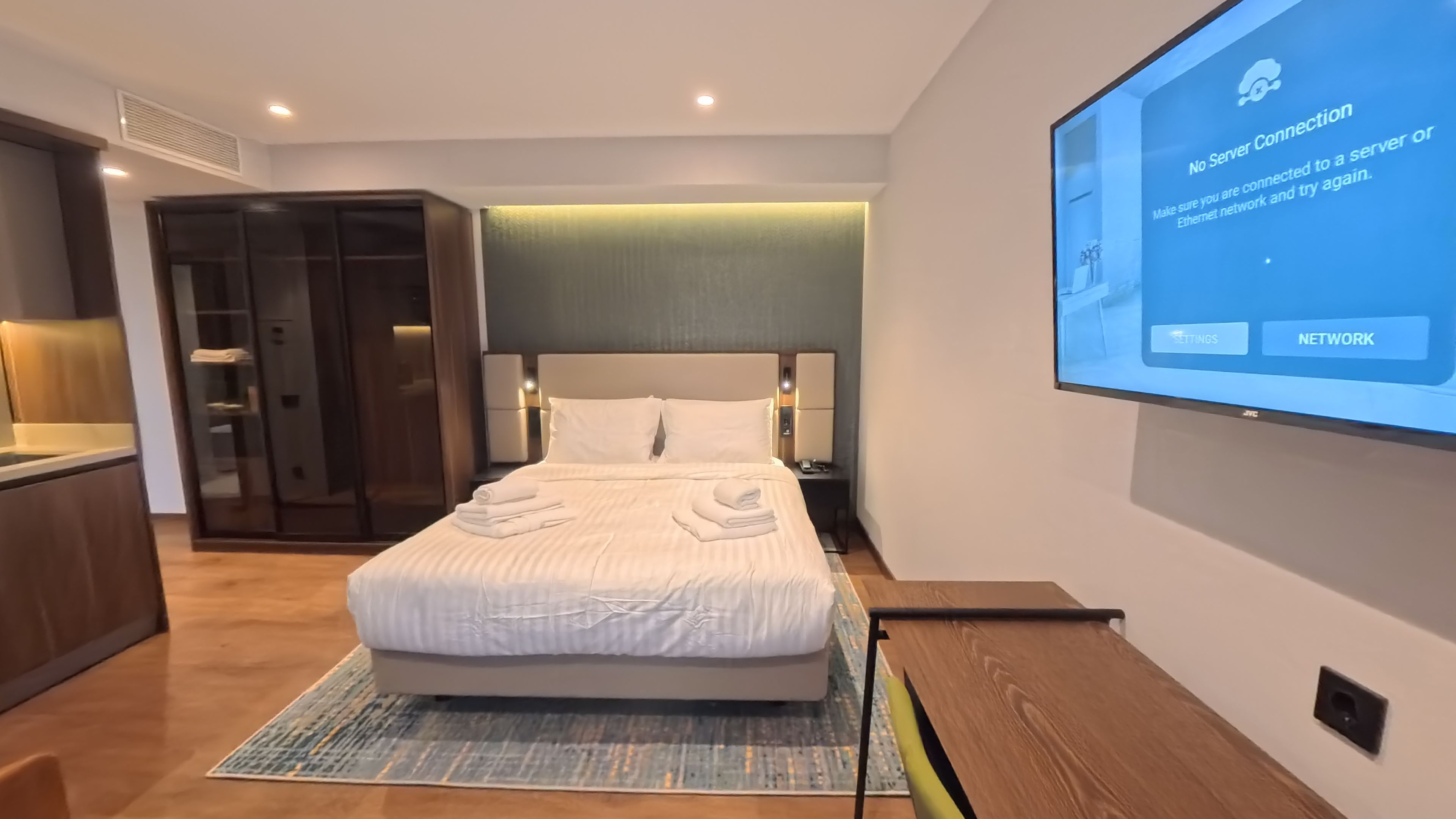 Una habitación de hotel con cama, un televisor mostrando el mensaje 'No hay conexión al servidor', un armario y una mesita de noche.